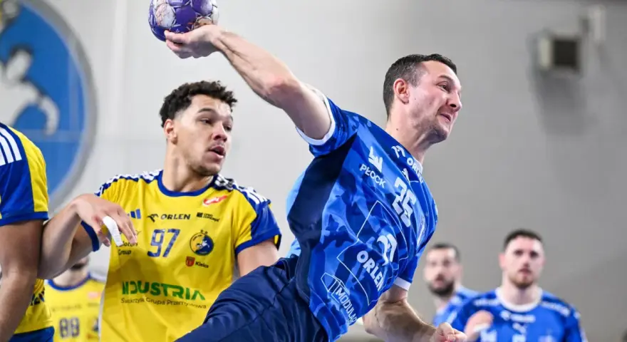 Gracz w niebieskiej koszulce rzuca piłkę, podczas gdy przeciwnik w żółtej koszulce z numerem 97 próbuje go zablokować. Emocjonujący mecz piłka ręczna liga mistrzów.