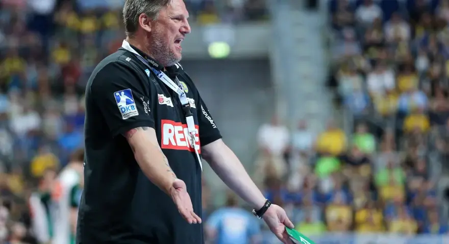 Trener Nikolaj Jacobsen w czarnej koszulce z logo DKB, gestykuluje na tle trybun pełnych kibiców.