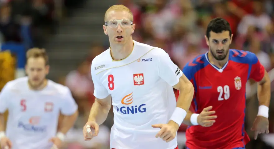 Kamil Bielecki w okularach ochronnych, z numerem 8 na koszulce, biegnie podczas meczu. Obok zawodnik z numerem 29.