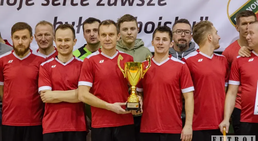 Drużyna w czerwonych koszulkach świętuje zwycięstwo z pucharem. W centrum stoi Andrzej Zaborowski, dumny z sukcesu.