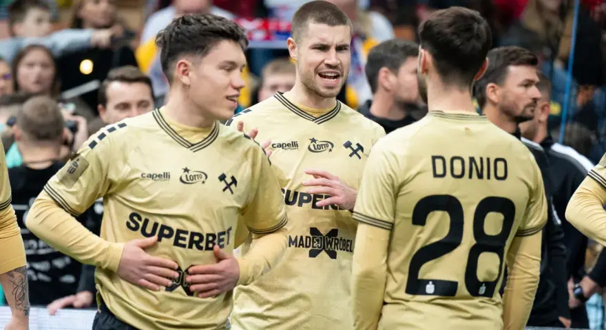 Piłkarze ręczni Górnika Zabrze w złotych strojach rozmawiają na boisku.