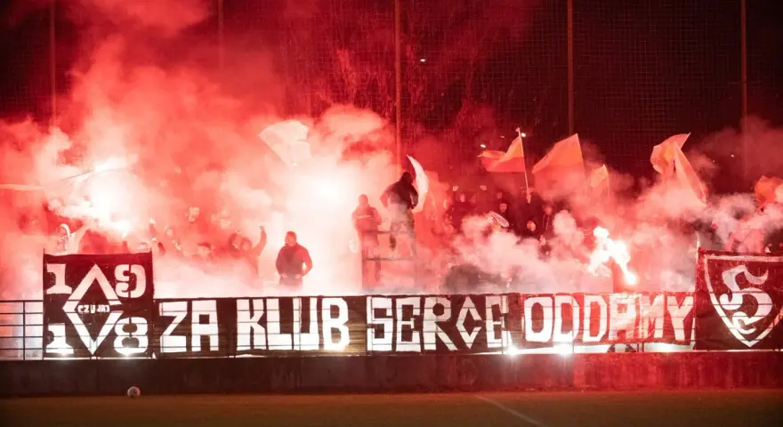 Fani z piłą ręczną, czuwaj przemyśl! Tłum kibiców z racami i flagami tworzy czerwony dym.