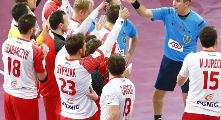 Polska kadra piłka ręczna świętuje zwycięstwo. Zawodnicy w białych strojach z czerwonymi detalami, z numerami 18, 23 i 15, cieszą się z sukcesu.