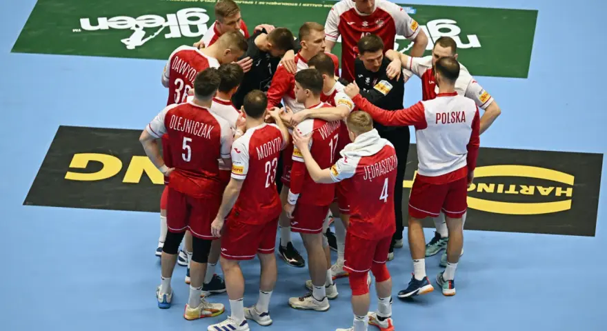 Drużyna piłkarzy ręcznych Polski w czerwonych strojach z białymi detalami, zjednoczona w kółku. To kluczowy moment przed meczem, być może decydującym o dalszych losach w mistrzostwach świata.