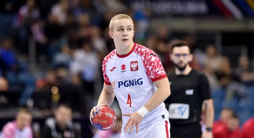 Młody zawodnik w białej koszulce z orłem i numerem 4, gotowy do rzutu piłką ręczną.