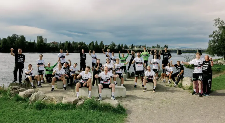 Drużyna Elverum Handball świętuje nad rzeką, pozując do wspólnego zdjęcia w sportowych strojach.