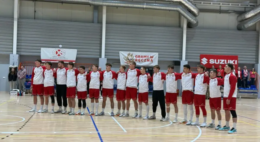 Drużyna w strojach biało-czerwonych, w tym Filip Jankowski, stoi na parkiecie hali sportowej.