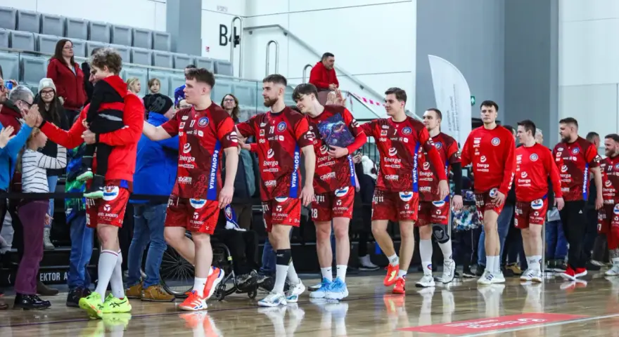 Drużyna kwidzyn piłka ręczna w czerwonych strojach wchodzi na halę, pozdrawiając kibiców.