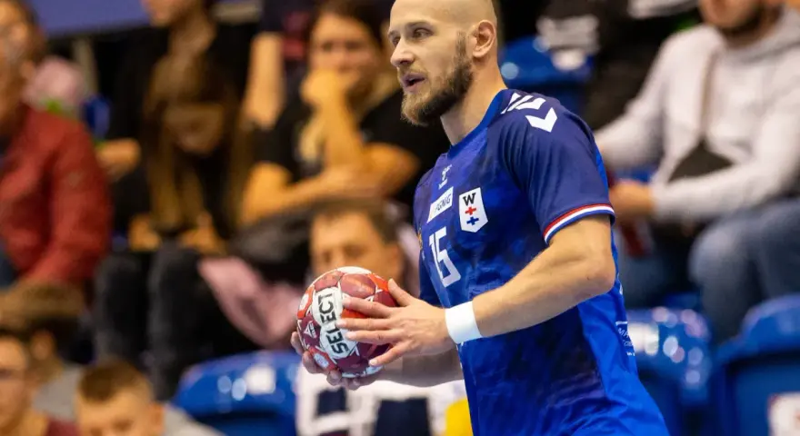 Mateusz Jachlewski, szczypiornista w niebieskiej koszulce z numerem 15, trzyma piłkę do piłki ręcznej.
