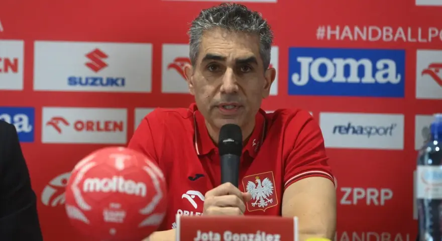 Jota González, trener reprezentacji Polski w piłce ręcznej, przemawia do mikrofonu. Obok niego czerwona piłka.