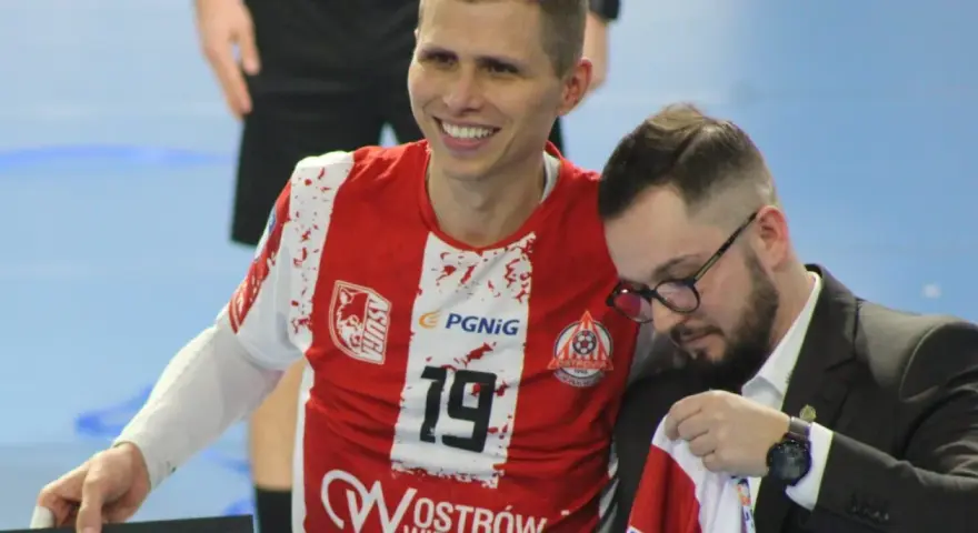 Uśmiechnięty Bartłomiej Tomczak w czerwonej koszulce z numerem 19, obok niego mężczyzna w garniturze.