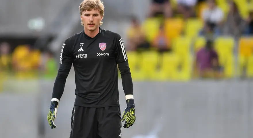 Mateusz Zych, bramkarz w czarnej koszulce z numerem 77, gotowy do akcji na boisku.