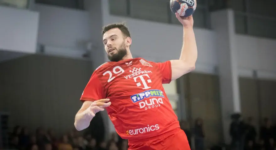 Piłkarz ręczny Nedim Remili w czerwonej koszulce z numerem 29, z piłką w dłoni, gotowy do rzutu.