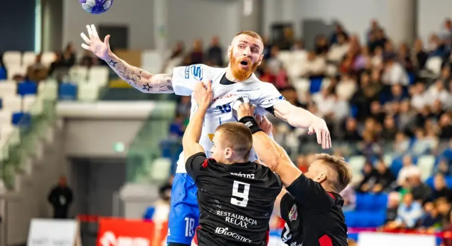 Jakub Wolski w akcji, walczy o piłkę w powietrzu z dwoma przeciwnikami.