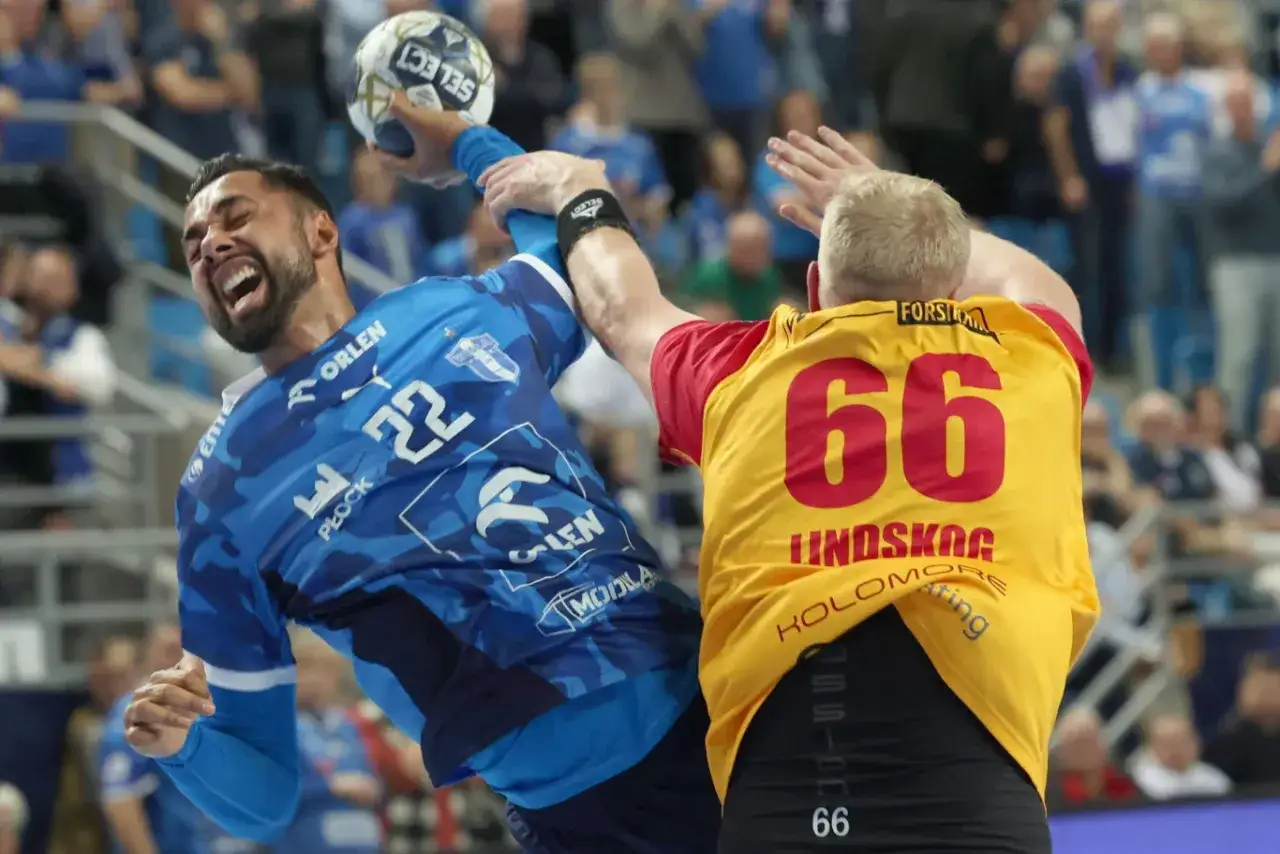 Gracz gog handball w niebieskiej koszulce z numerem 22 rzuca piłkę, blokowany przez przeciwnika w ż&oacute;łtej koszulce z numerem 66.