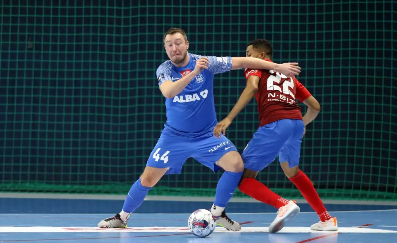 Jakub Grzybowski w akcji, walczy o piłkę z przeciwnikiem na boisku futsalowym.