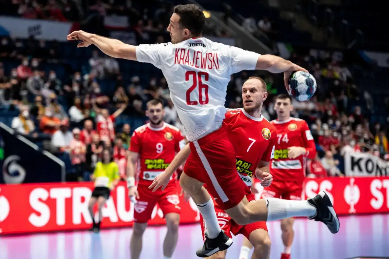 Piłkarz w skoku do rzutu podczas mistrzostw w piłce ręcznej. Zawodnik z numerem 26 na plecach, Krajewski, celuje do bramki.