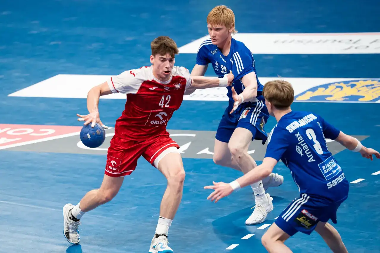 Jakub Kozłowski w akcji na boisku do piłki ręcznej, w białej koszulce z numerem 42, próbuje przejąć piłkę.