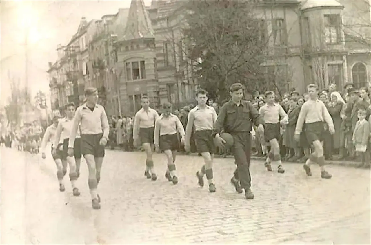 Młodzi mężczyźni w strojach sportowych, być może drużyna Zagłębia Lubin piłka ręczna mężczyzn, maszerują ulicą.