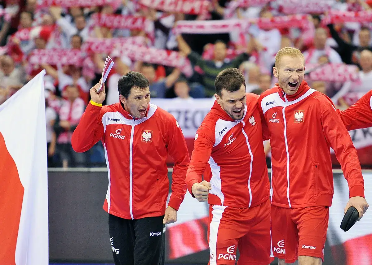 Trzech zawodników w czerwonych strojach świętuje sukces w lidze piłki ręcznej.