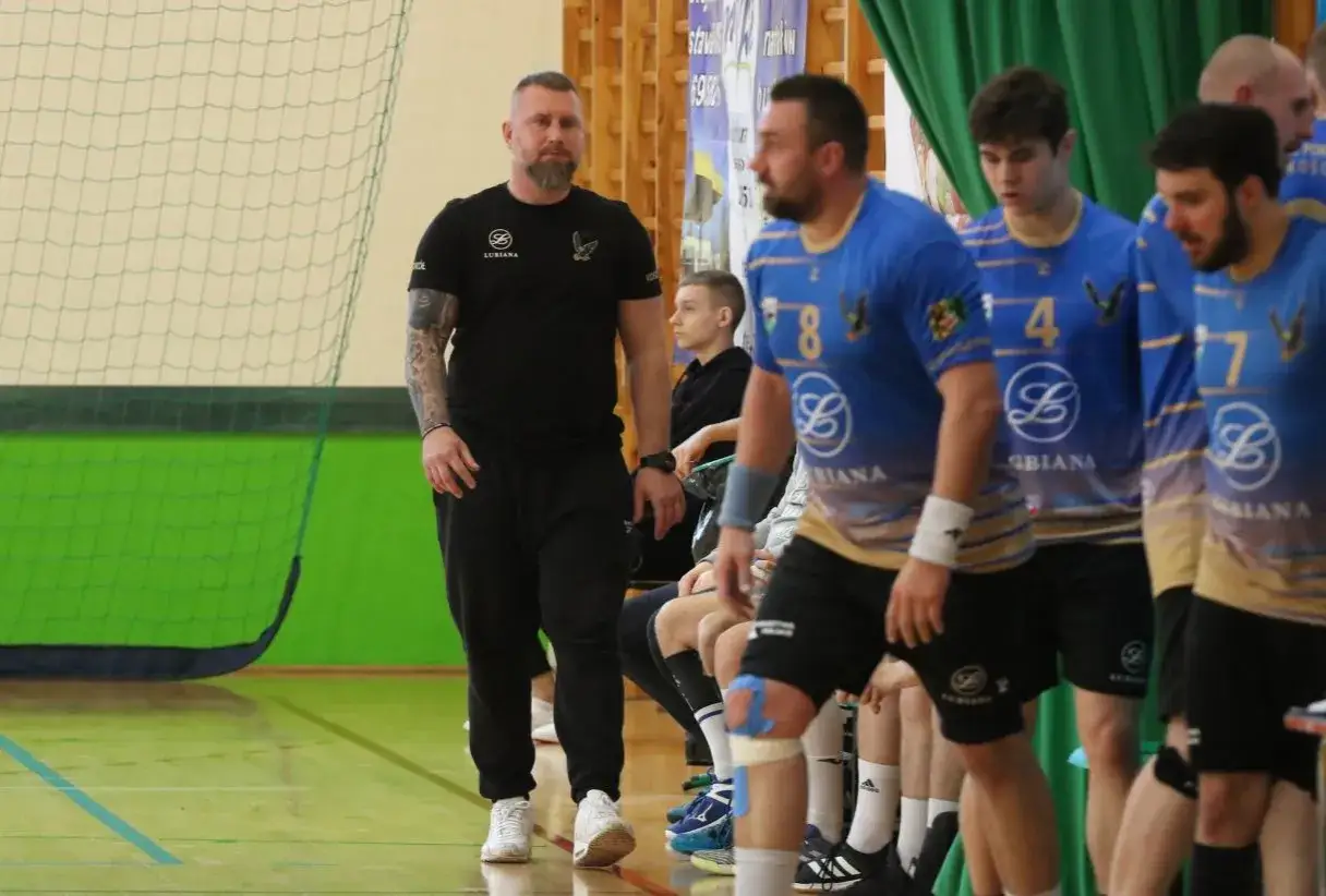 Maciej Reichel, trener, obserwuje mecz. Obok niego siedzą zawodnicy w niebieskich koszulkach.
