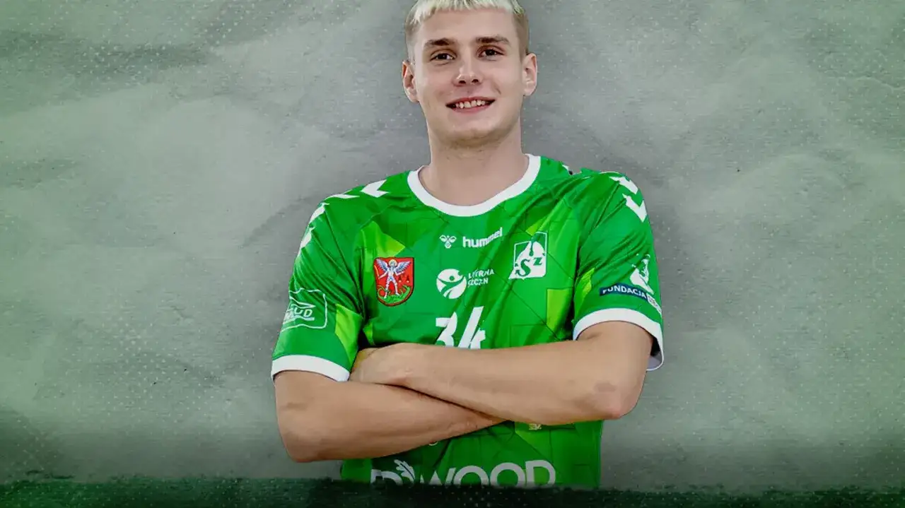 Bartosz Andrzejewski w zielonej koszulce z numerem 24, z rękami skrzyżowanymi na piersi, uśmiecha się do obiektywu.