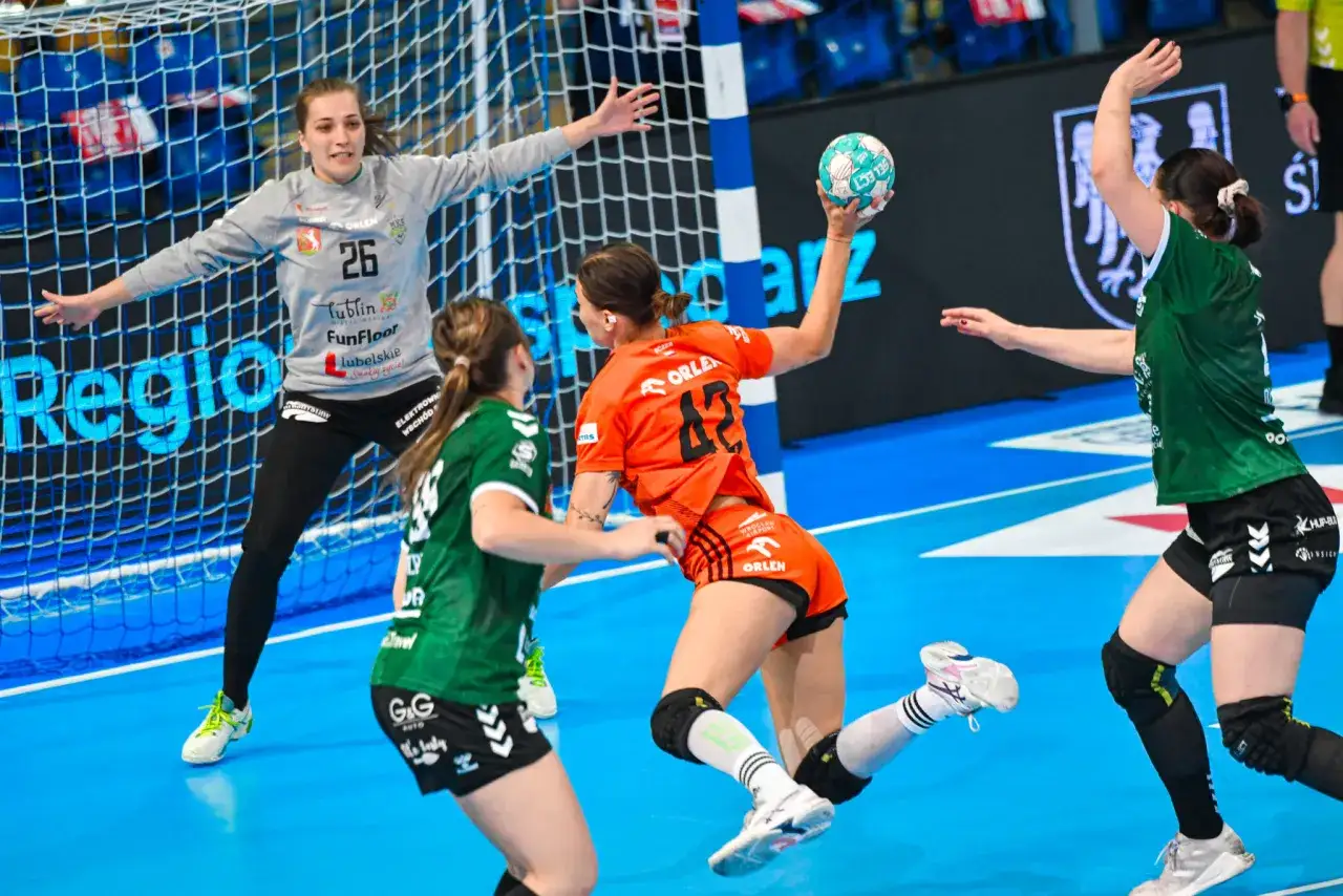 Piłkarki ręczne w akcji, bramkarka w szarym stroju broni, a zawodniczka w pomarańczowym rzuca piłkę. Mecze europejskiej federacji piłki ręcznej to emocje!