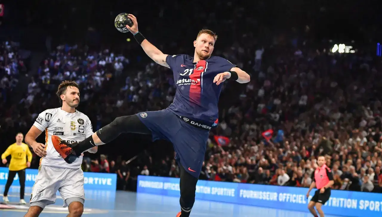 Gracz PSG w skoku do rzutu podczas meczu piłki ręcznej. W tle trybuny pełne kibiców.