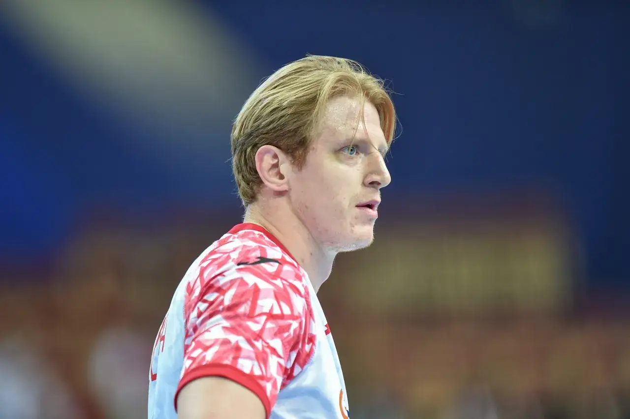 Tomasz Gębala, szczypiornista w białej koszulce z czerwonym wzorem, patrzy w bok z determinacją.