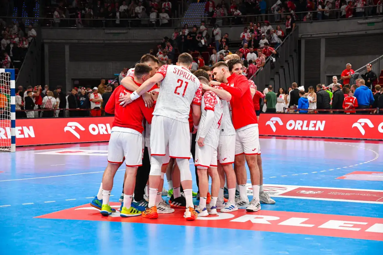 Drużyna piłkarzy ręcznych w białych strojach z czerwonymi detalami tworzy zgraną grupę. To ważny moment podczas mistrzostw świata w piłce ręcznej.