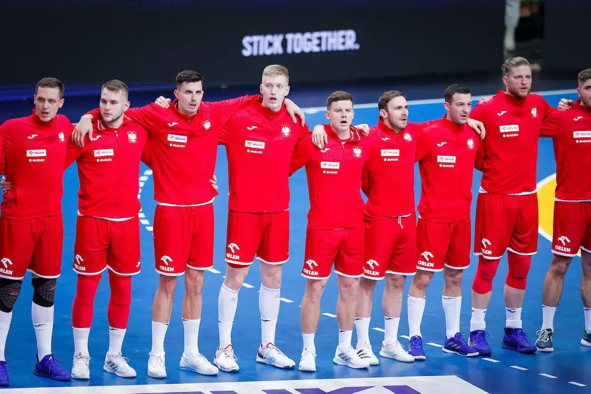 Reprezentacja Polski w piłce ręcznej mężczyzn w czerwonych strojach, z ramionami na barkach, gotowa do walki.