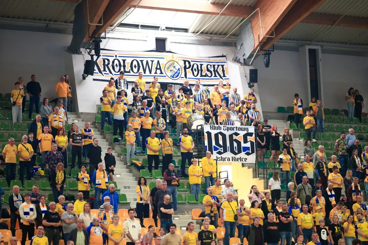 Kibice na meczu Iskra Kielce dopingują swoją drużynę. Wszyscy ubrani w żółto-niebieskie barwy, z transparentem