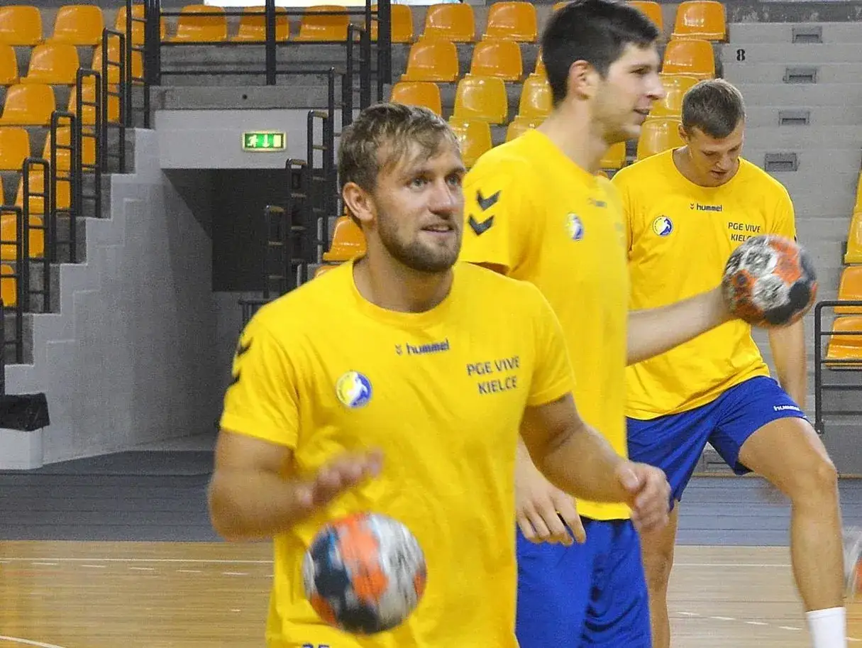 Luka Cindrić w żółtej koszulce PGE Vive Kielce ćwiczy rzuty piłką ręczną na hali sportowej.