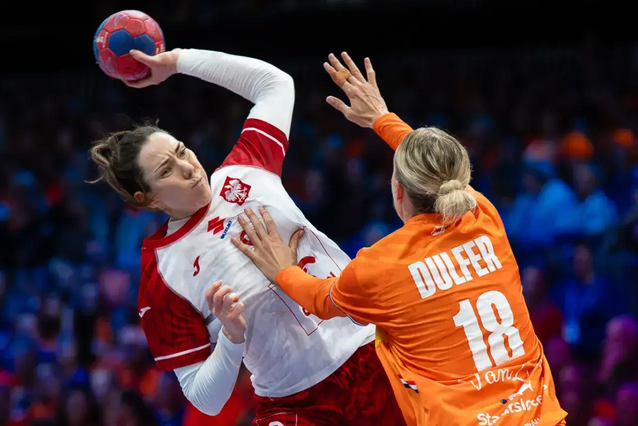 Piłka ręczna mistrzostwa: zawodniczka w białej koszulce z orłem próbuje rzucić piłkę, blokowana przez przeciwniczkę w pomarańczowej koszulce z numerem 18.