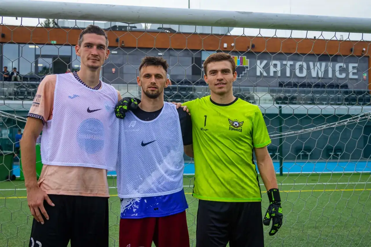 Trzech piłkarzy w strojach treningowych pozuje do zdjęcia. Zgrupowanie kadry przed meczem.
