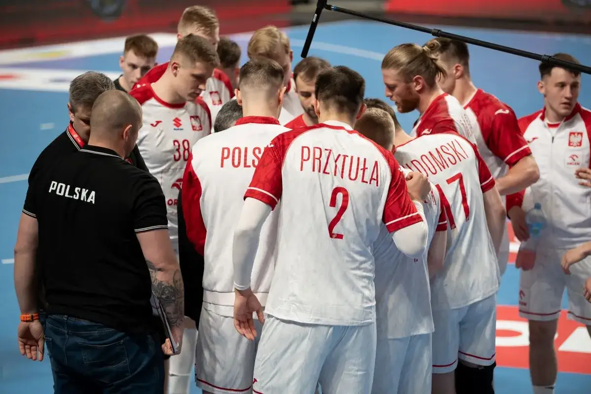 Drużyna piłki ręcznej Polska w białych strojach z czerwonymi detalami, w skupieniu przed meczem z Włochami.