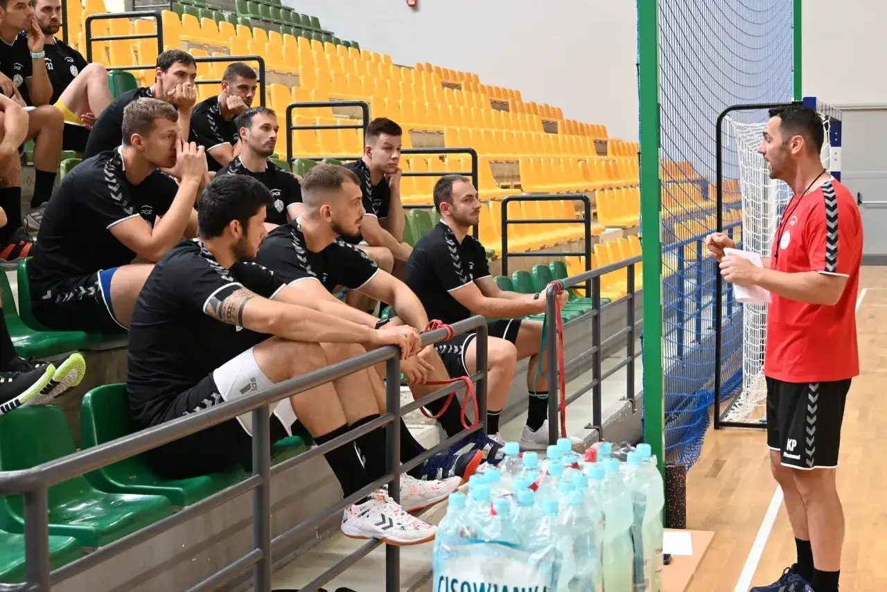 Trener Vive Kielce w czerwonej koszulce przemawia do zawodników siedzących na trybunach.