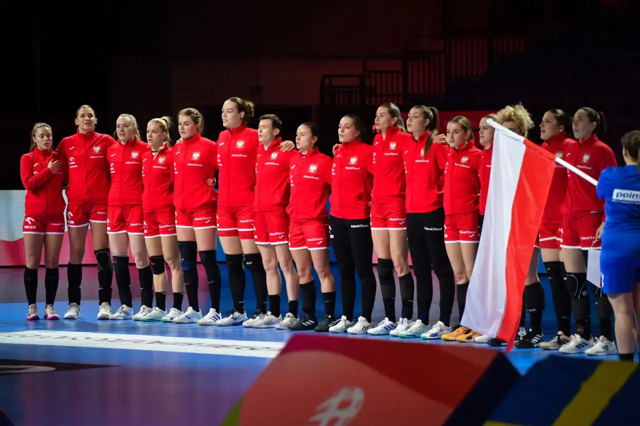 Drużyna Polski w piłce ręcznej w czerwonych strojach, z flagą narodową.