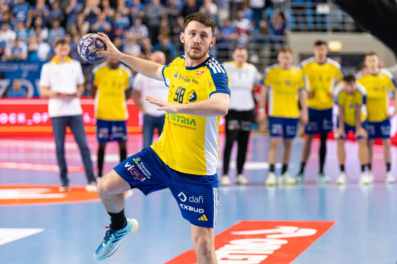 Piłkarz ręczny Vive Kielce z piłką, gotowy do rzutu. Kibice na trybunach czekają na Ligę Mistrz&oacute;w. Sprawdźcie terminarz!