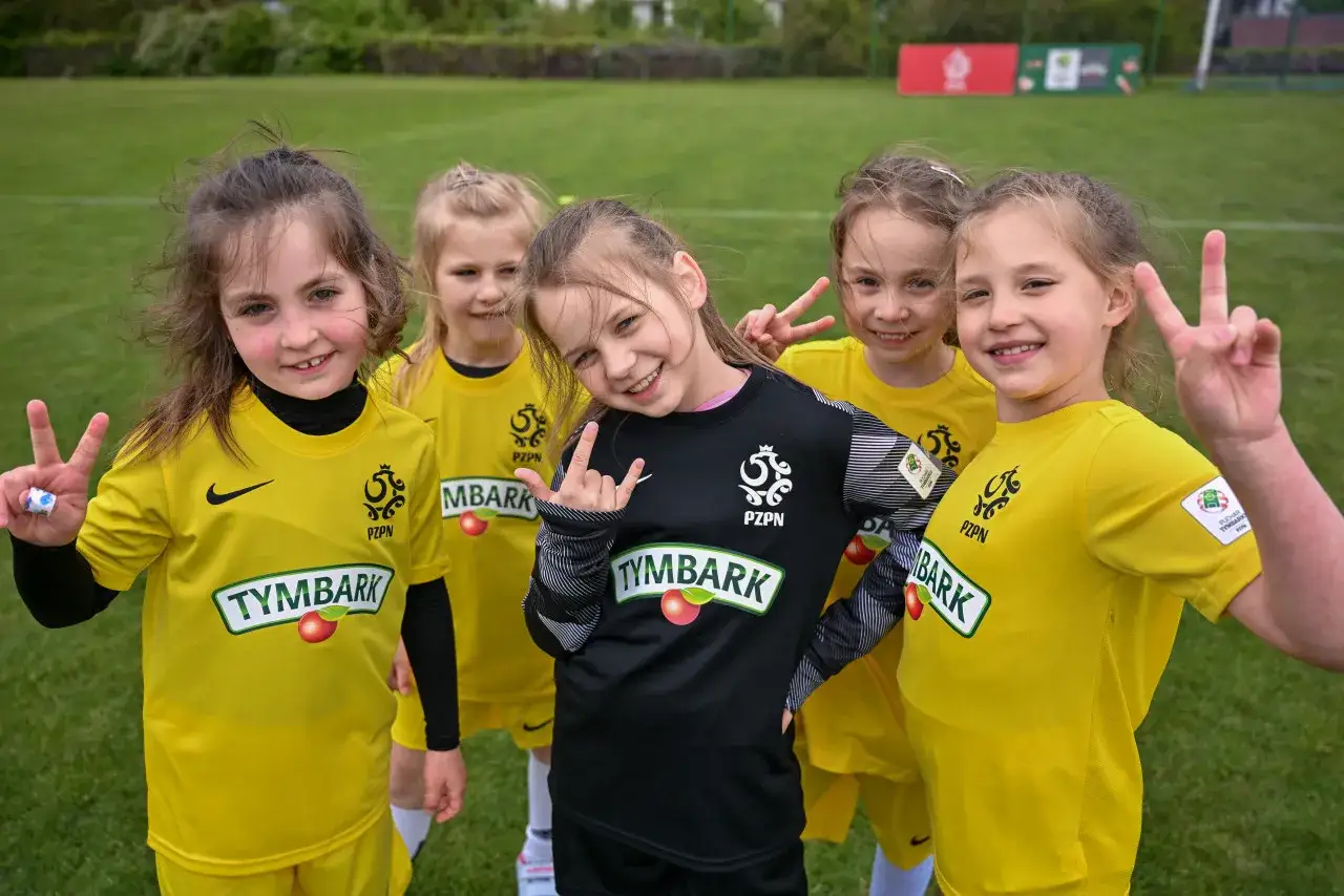 Uśmiechnięte dziewczynki w ż&oacute;łtych strojach piłkarskich, gotowe do gry w mistrzostwa polski junior&oacute;w.