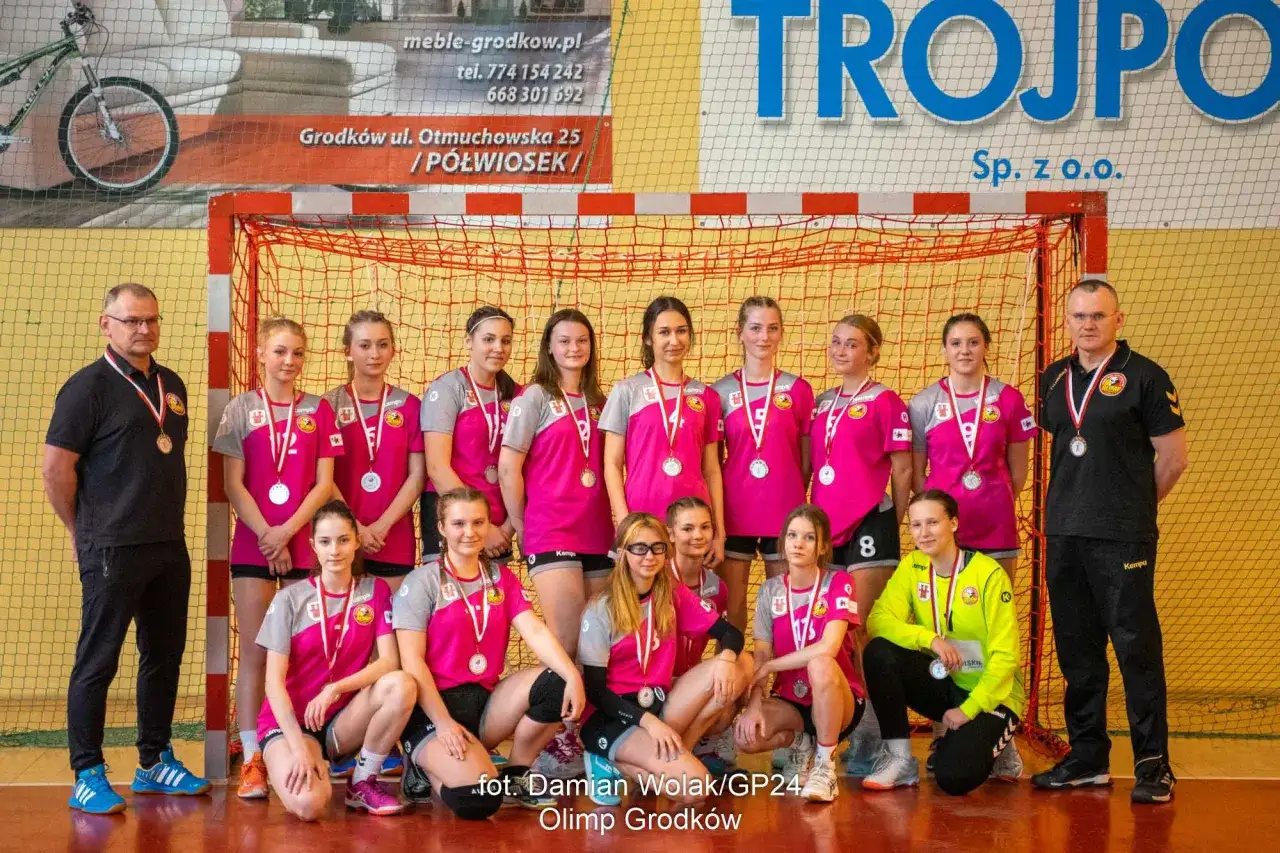 Drużyna piłki ręcznej Olimp Grodków z trenerem i medalami po zwycięstwie.