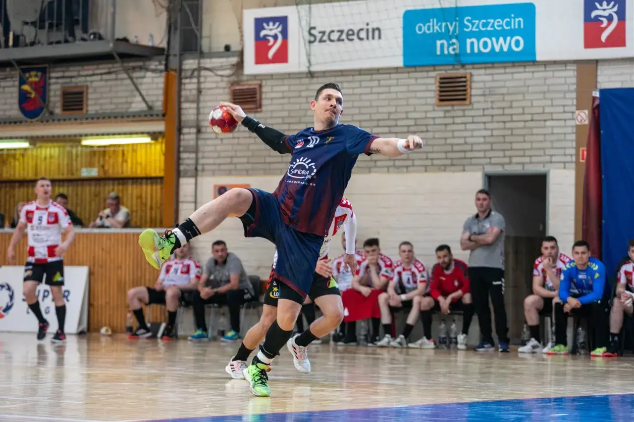 Tomasz Zaręba w skoku rzuca piłką ręczną. Zawodnik w niebiesko-bordowym stroju z numerem 10 na koszulce.