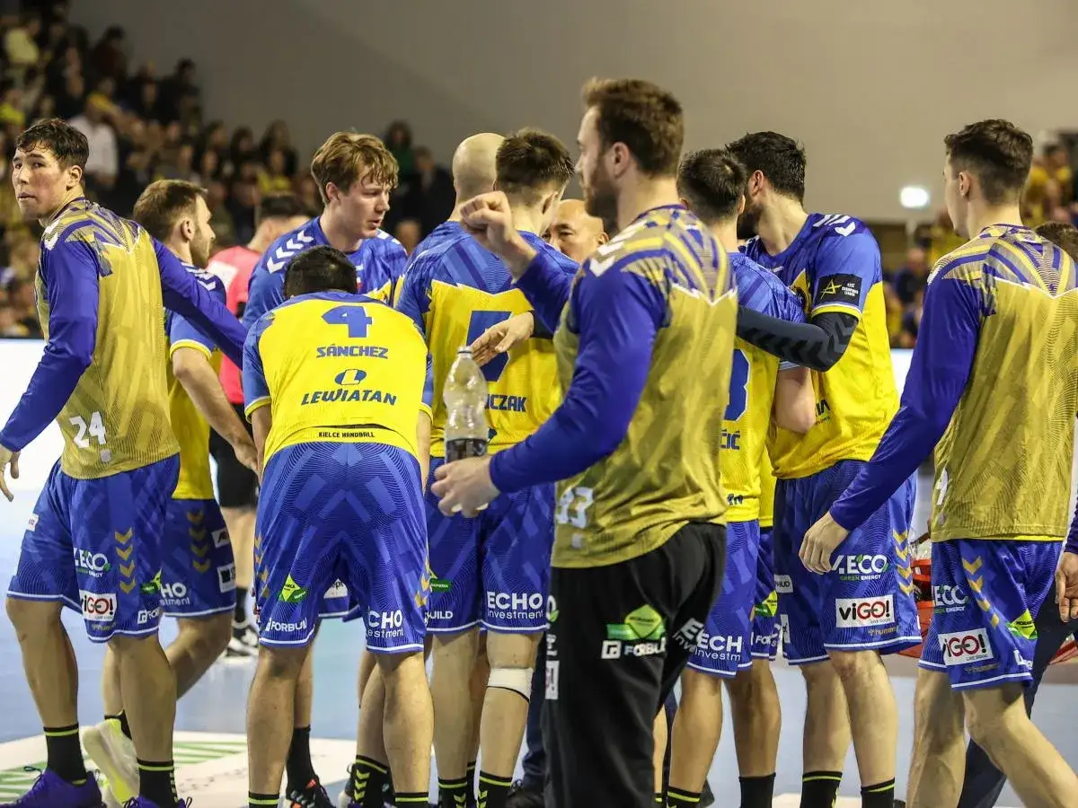 Drużyna Vive Kielce w żółto-niebieskich strojach, zawodnicy rozmawiają między sobą, jeden z nich trzyma butelkę wody.