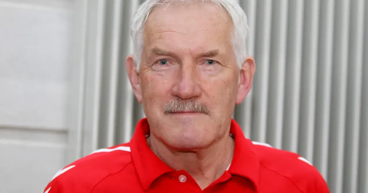 Portret starszego mężczyzny z siwymi włosami i wąsami, ubranego w czerwoną koszulkę. To Zygfryd Kuchta, znany trener.
