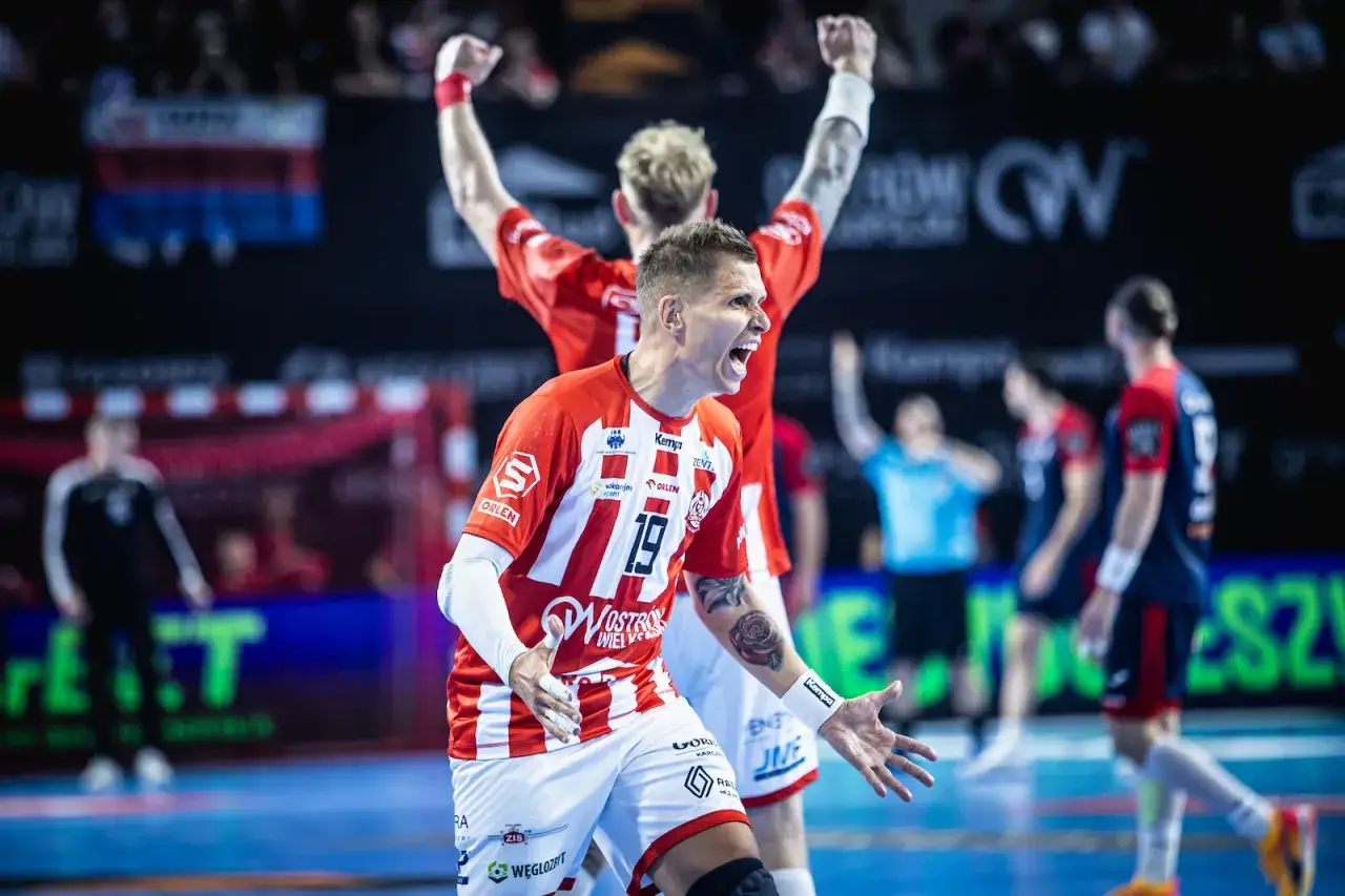 Bartłomiej Tomczak świętuje zdobycie bramki, krzycząc z radości. Jego drużyna w czerwono-białych strojach triumfuje na boisku.