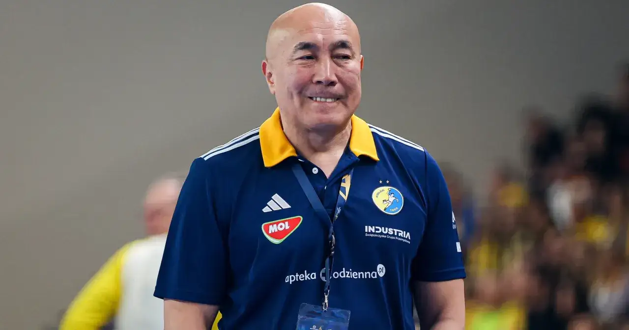 Uśmiechnięty trener Vive Kielce w granatowej koszulce z żółtym kołnierzem, z logo klubu na piersi.