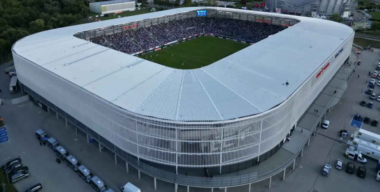 Widok z lotu ptaka na stadion podczas meczu w Płocku. Tłumy kibiców na trybunach, zielona murawa i nowoczesna architektura obiektu.