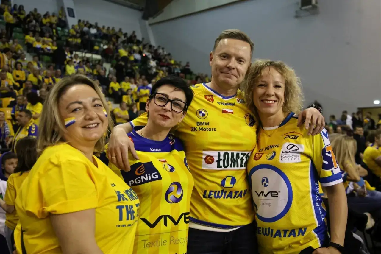 Uśmiechnięci kibice w żółtych koszulkach z logo VIVE Kielce, wspierający swoją drużynę na meczu.