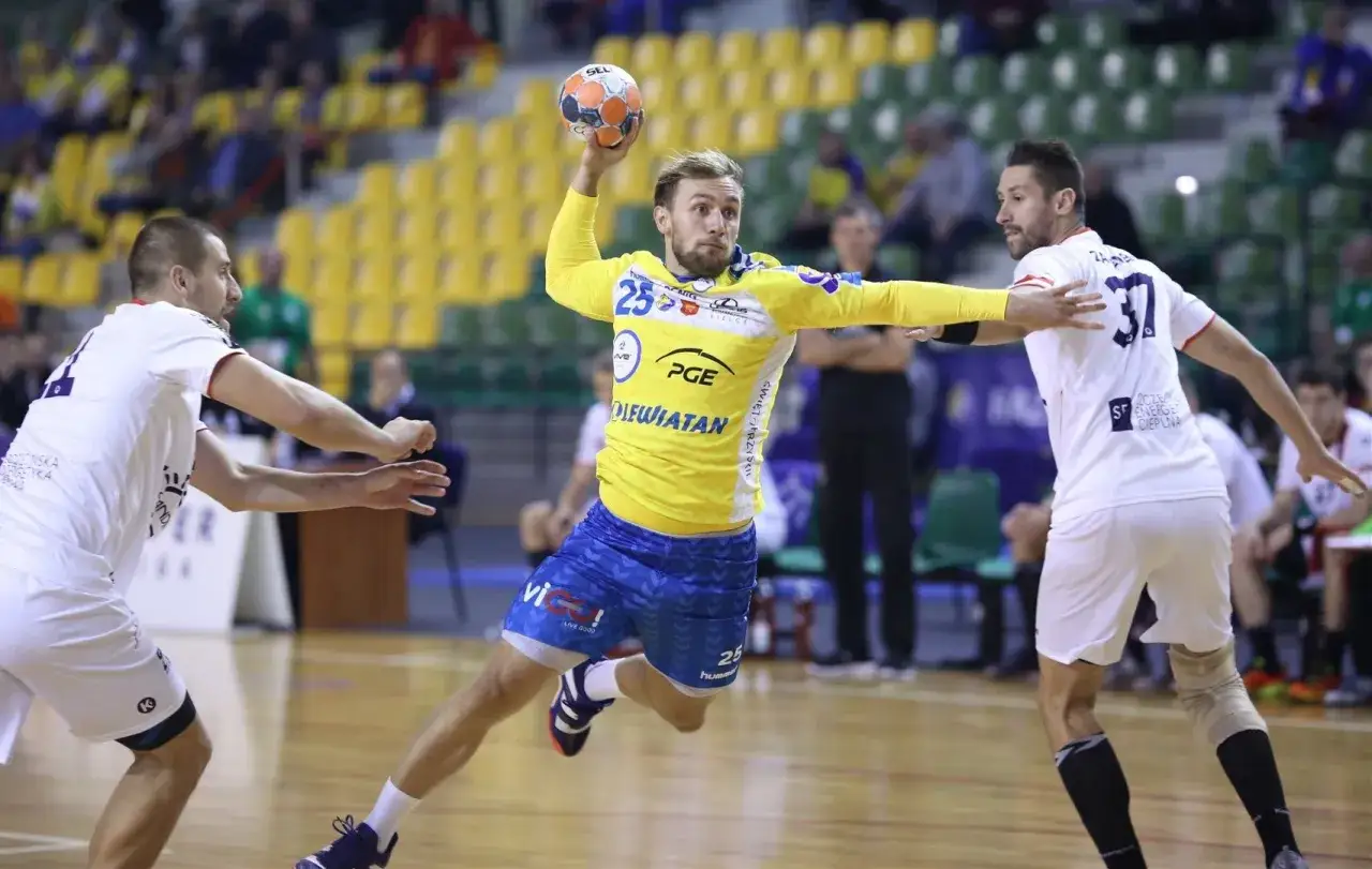 Luka Cindrić w żółtej koszulce z numerem 25 rzuca piłkę do bramki, broniony przez przeciwnika w białej koszulce z numerem 37.