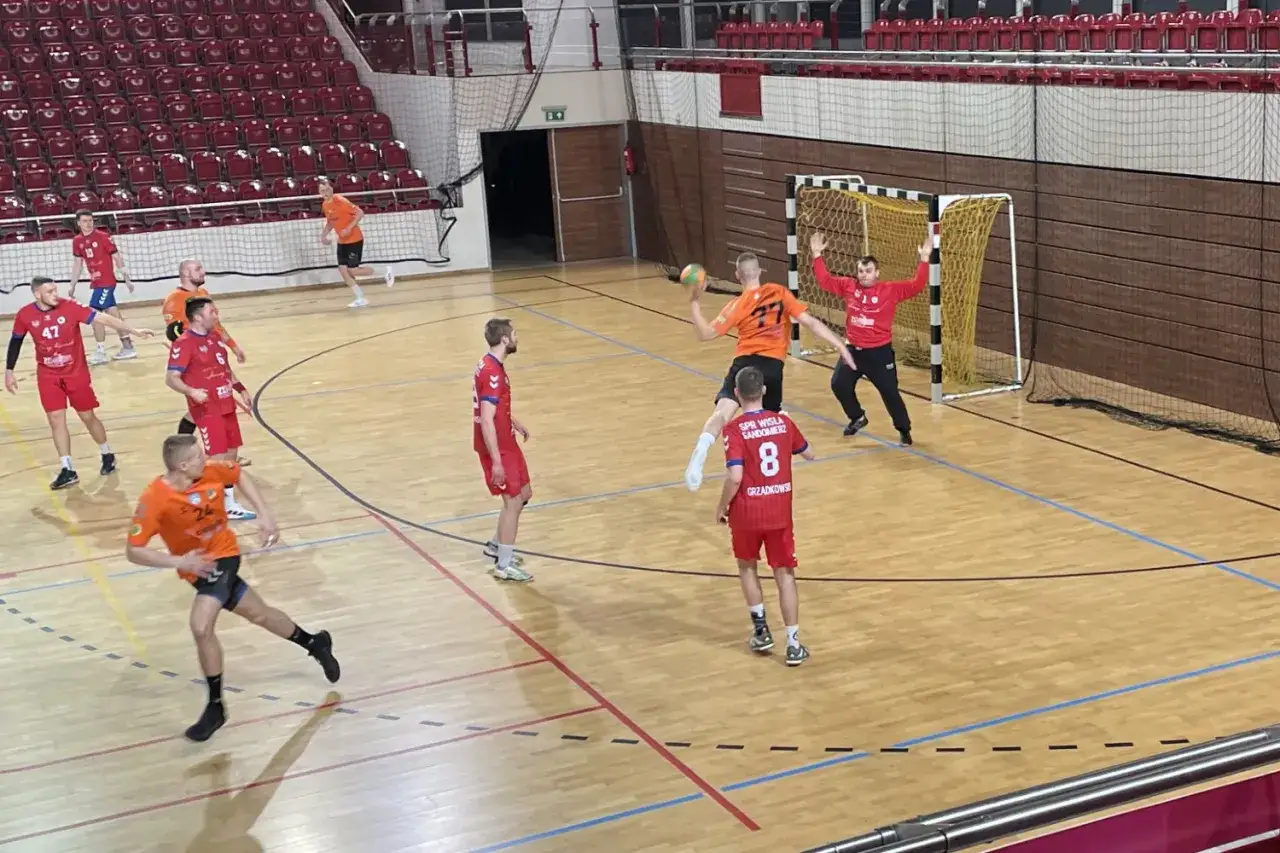 Mecz piłki ręcznej. Zawodnicy SPR Wisła Sandomierz w czerwonych strojach walczą o piłkę z przeciwnikami w pomarańczowych koszulkach.